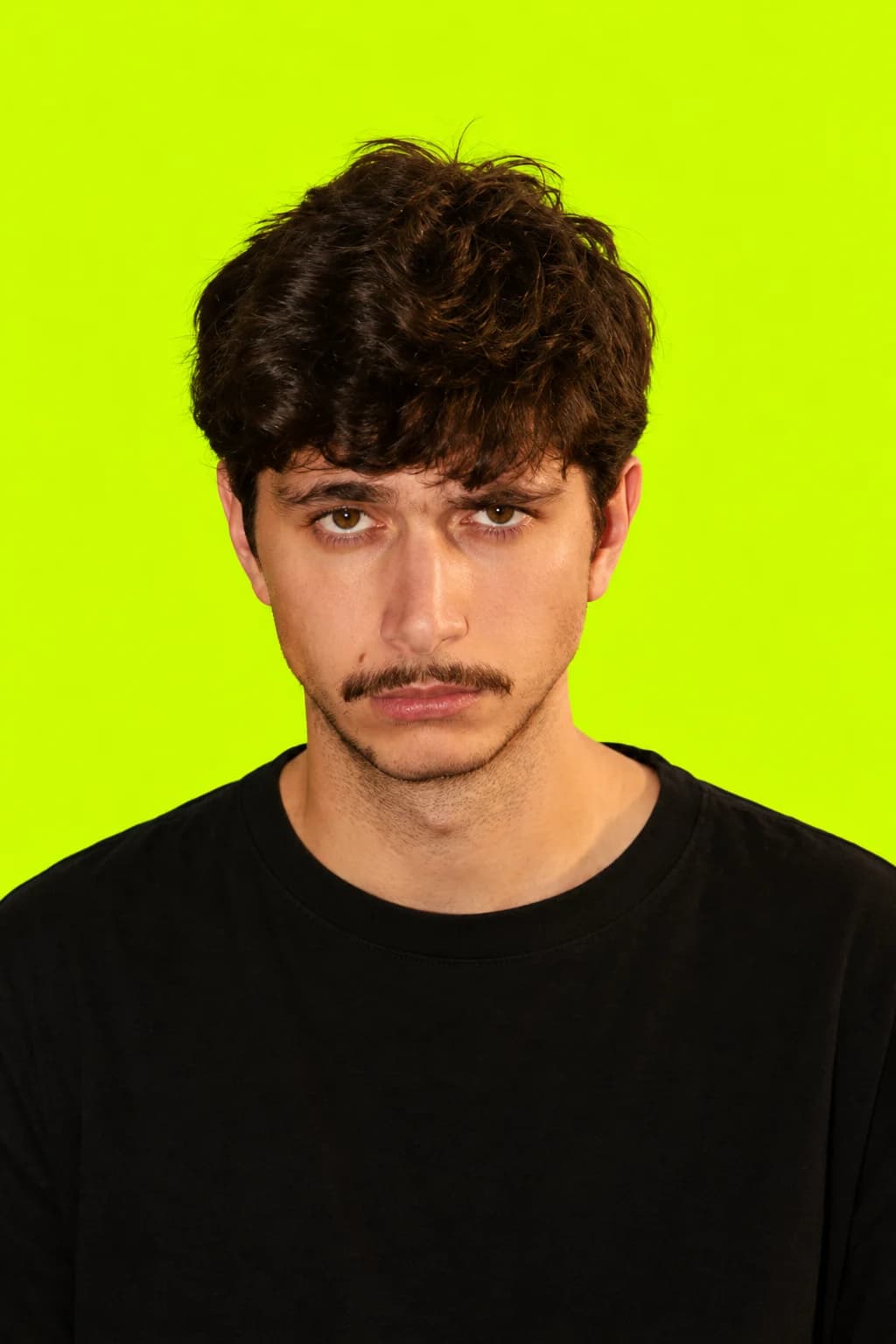 Retrato de Jota, con el pelo oscuro y camiseta negra, sobre el fondo verde lima de Tenderete