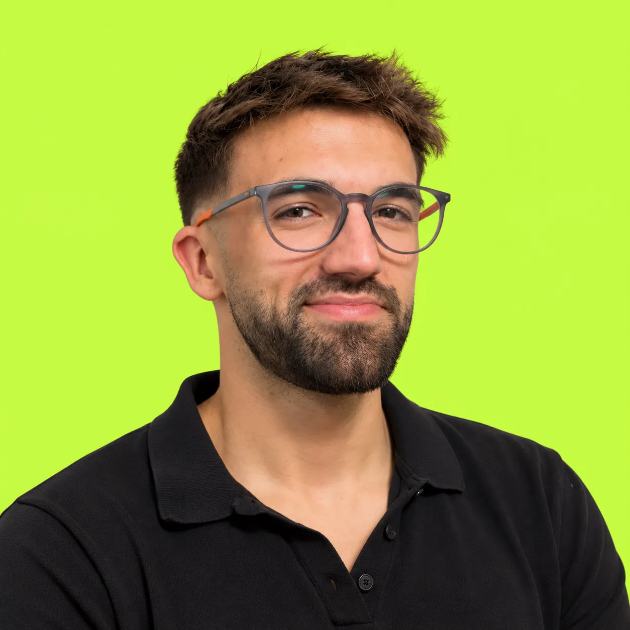 Retrato de Javier Wiott sonriendo, con gafas y polo negro, sobre fondo verde lima